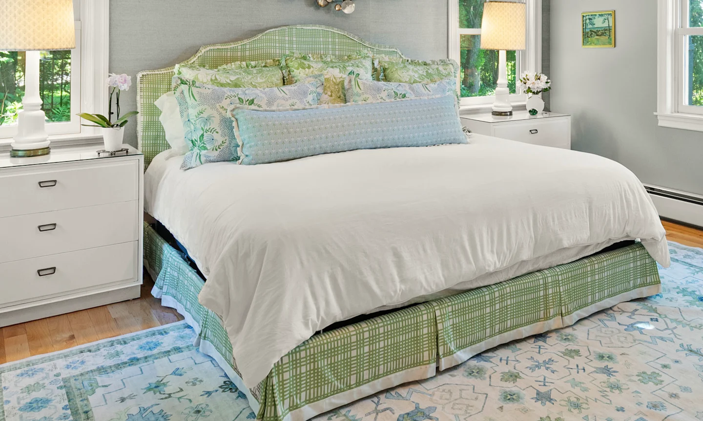 Bed with green upholstered headboard and skirt plus blue and green floral pillows.