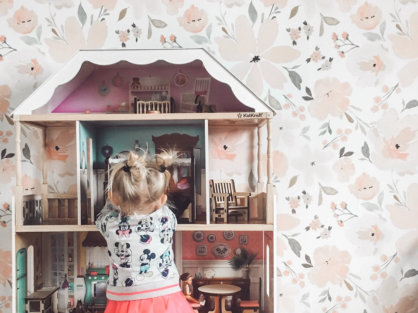 A little girl playing with a dollhouse in a room wallpapered with an IndyBloomDesigns floral print