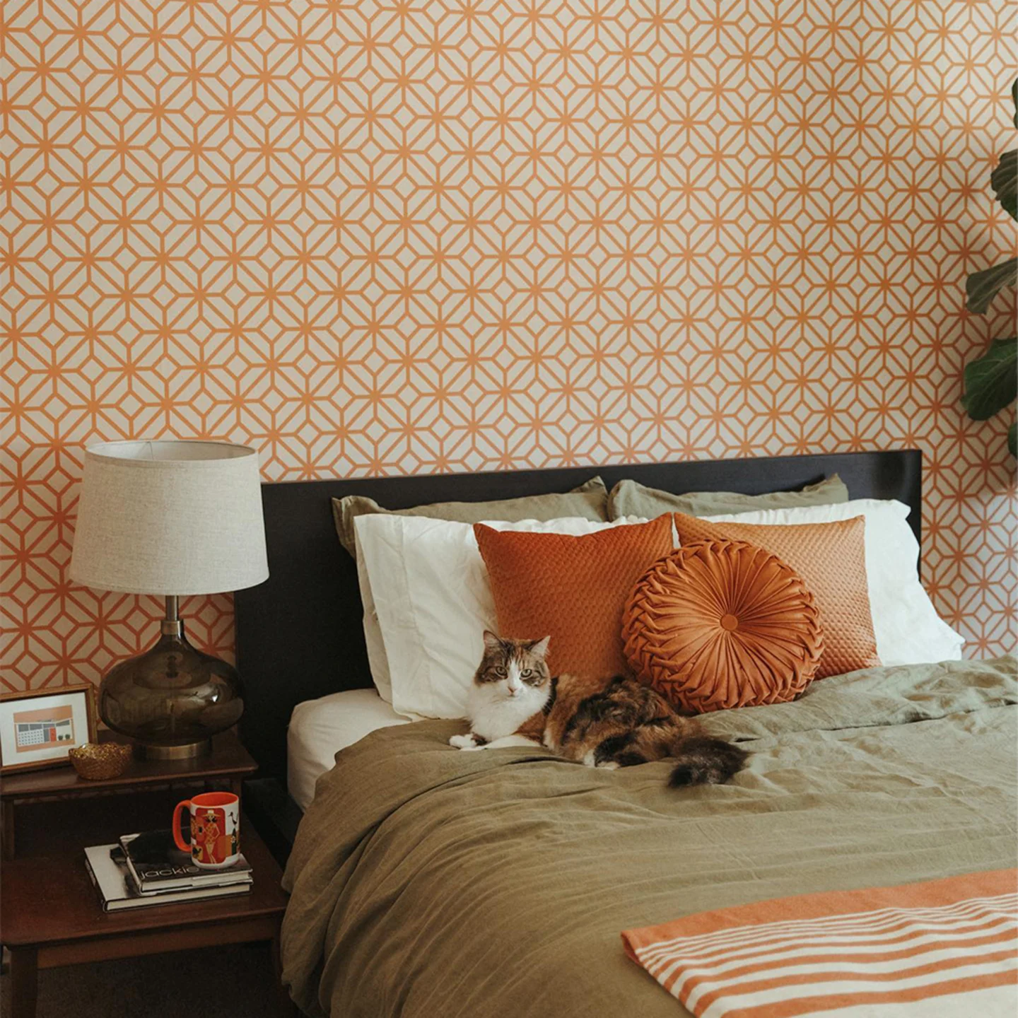 Orange geometric wallpaper behind a bed with a cat on it.